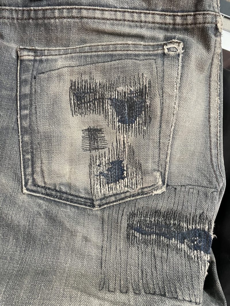 Darned and reinforced back pocket on faded grey jeans